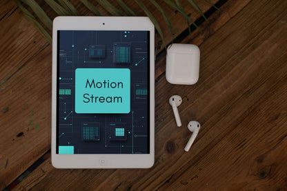 A tablet device displaying a motion stream graphic, placed on a wooden surface next to white wireless earbuds and their charging case.